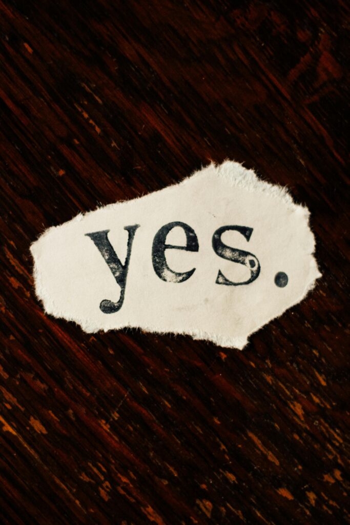 A rustic torn paper displaying the word 'yes' against a textured wooden background.